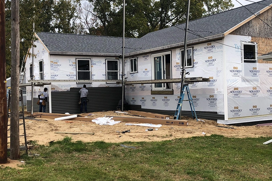 A residential home in Granger, IN, that is having house wrap applied under black siding that is being installed by two home improvement professionals.